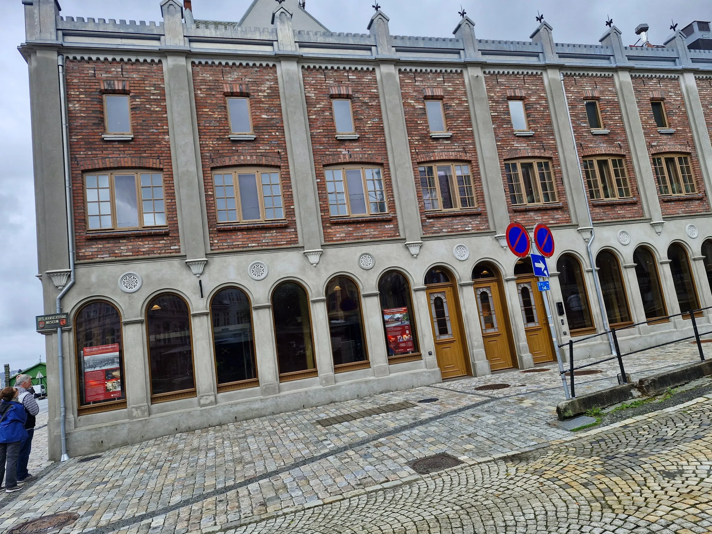 Teglfasade med vinduer, buede åpninger og dekor langs taket.